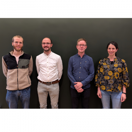 Die vier Kollegiatinnen stehen lächelnd nebeneinander vor einer olivgrünen Wand.