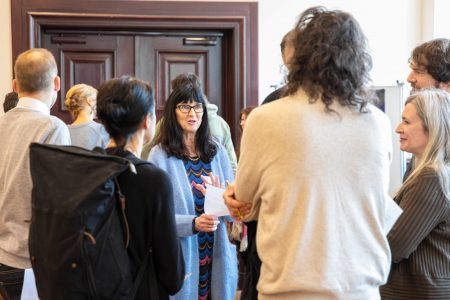 Teilnehmende im Austausch. Eine Gruppe von sechs Personen unterhält sich angeregt. Im Hintergrund stehen weitere Menschen.