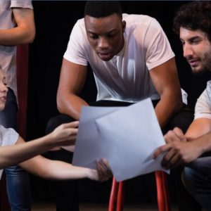 Sieben junge Menschen stehen auf einer Theaterbühne und erarbeiten gemeinsam den Text bzw. die Szene.