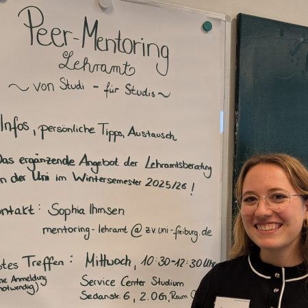 Die für das Peer-Mentoring zuständige Studentin steht lächelnd vor dem Plakat mit den Hinweisen zum Mentoring Angebot