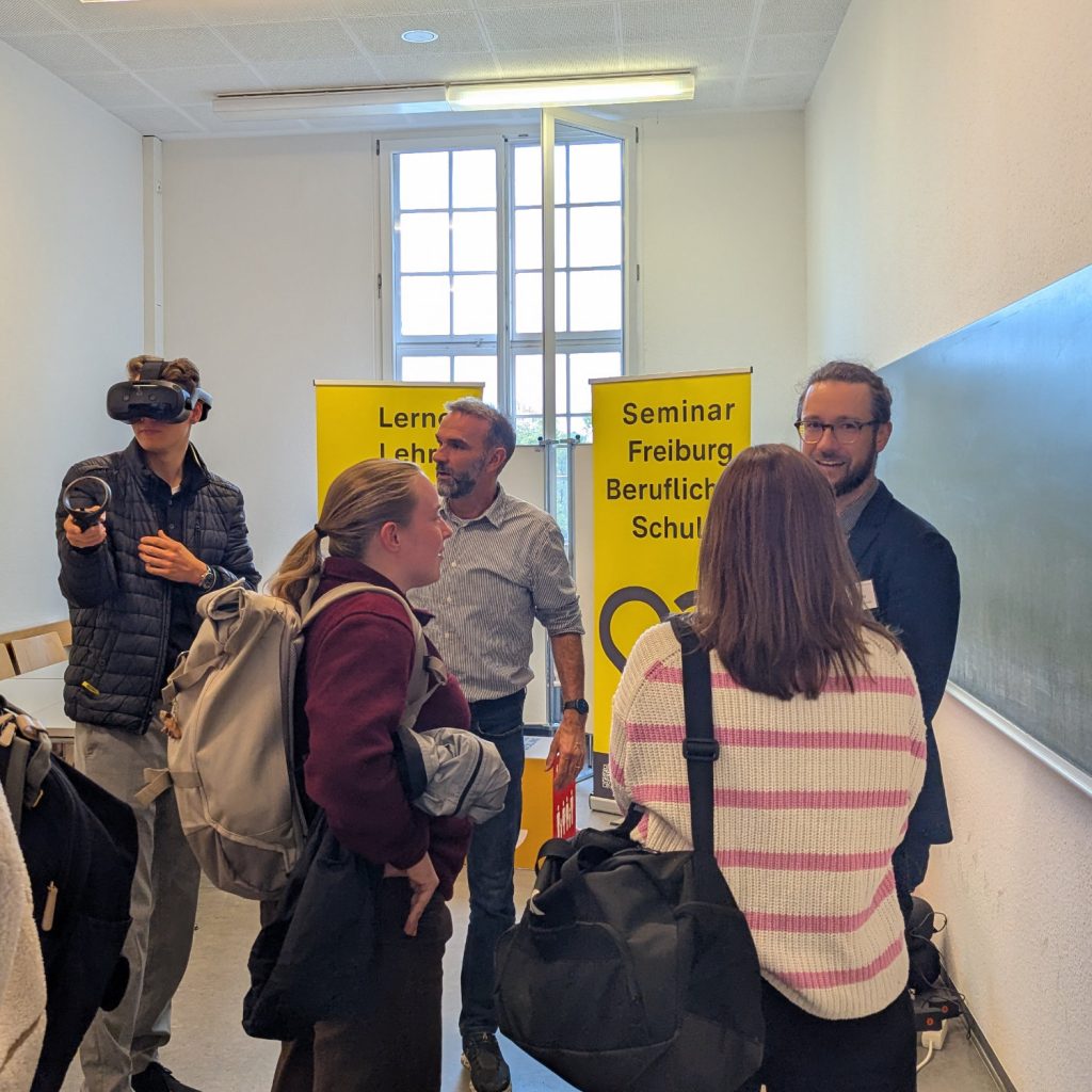 Studierende stehen bei einem Stand zu Beruflichen Schulen. Ein Student trägt eine VR Brille.