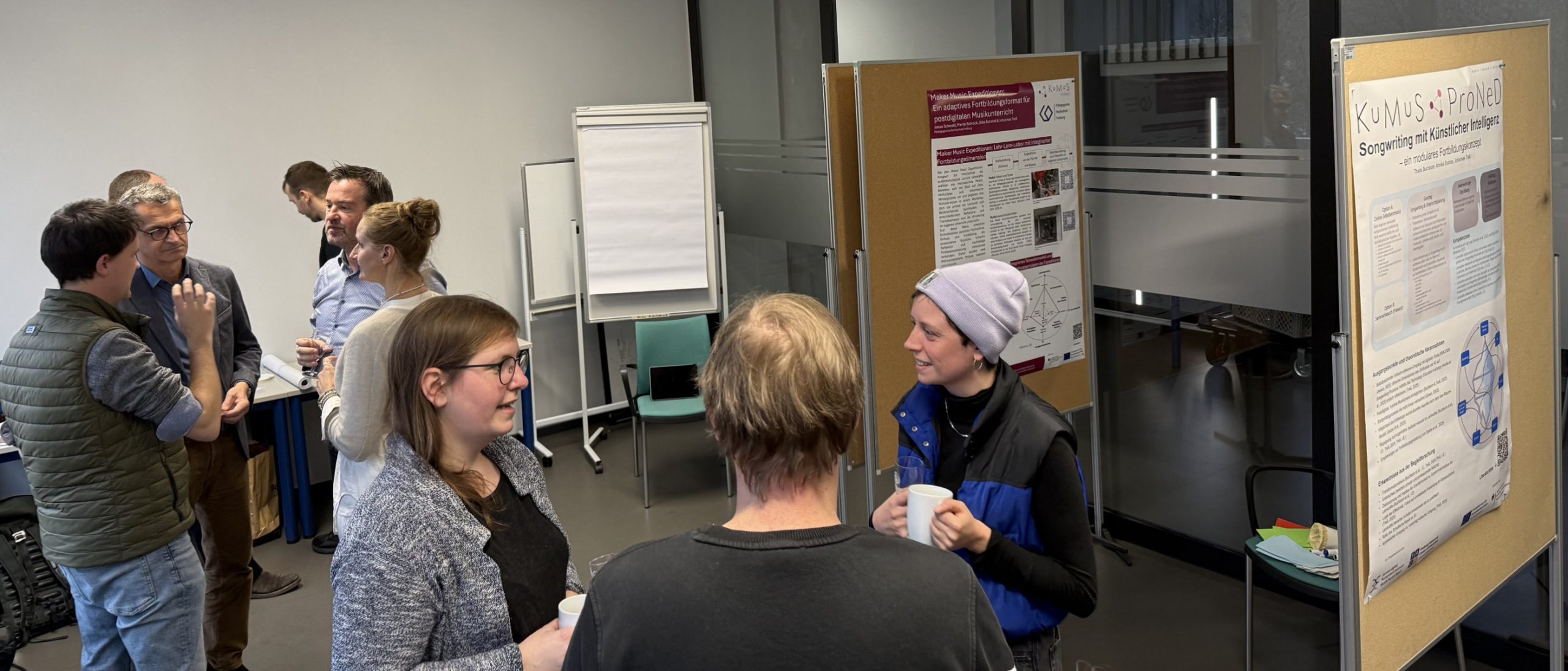 Mehrere Projektmitarbeitende stehen mit Getränken vor Posterwänden und unterhalten sich angeregt