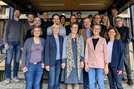 Nineteen participants of the meeting with the scientic advisory board meeting are standing together on the stairs before the meeting building and smile