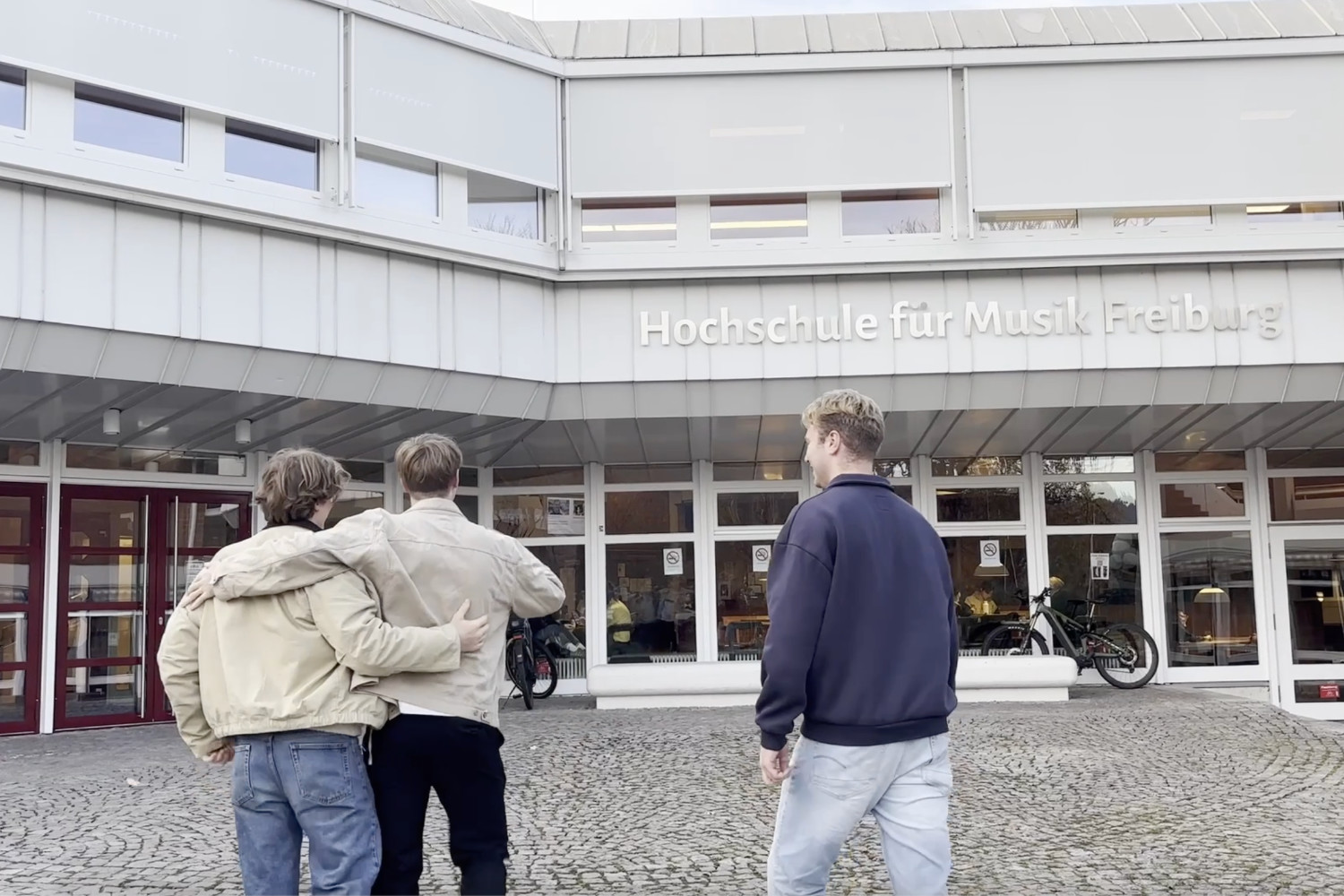 Drei männliche Studierende gehen gut gelaunt auf die Hochschule für Musik Freiburg zu