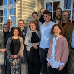 Die Teilnehmer*innen der Sitzung stehen lächelnd vor der Villa im Sonnenlicht