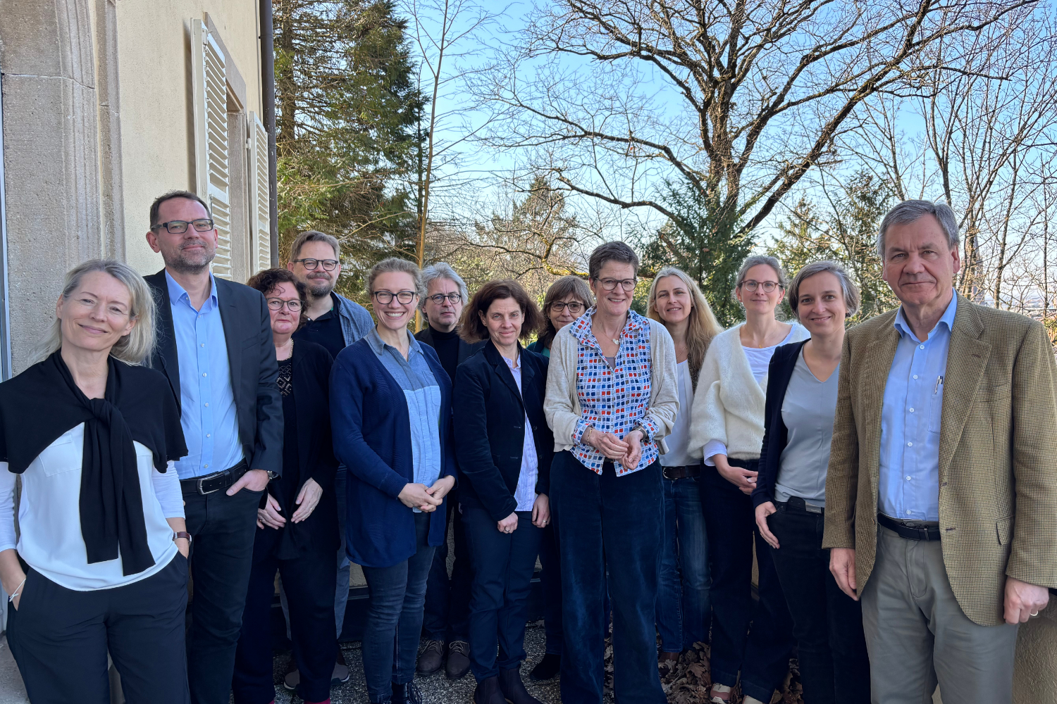 Die Teilnehmer*innen stehen lächelnd auf einem Balkon vor Bäumen