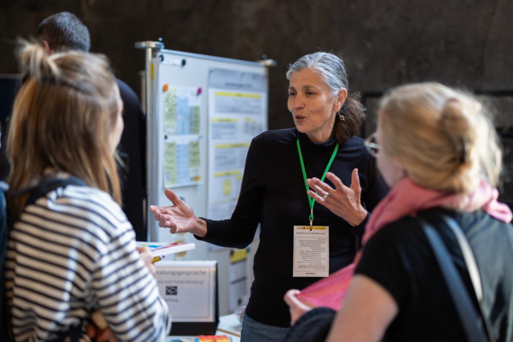 Zwei interessierte Junglehrerinnen tauschen sich an einem Infostand mit einer Frau von dem Stand aus.