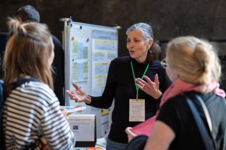 Zwei interessierte Junglehrerinnen tauschen sich an einem Infostand mit einer Frau von dem Stand aus.
