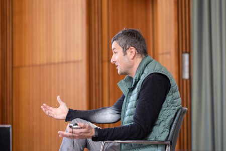 Andreas Kronenberg sitzt auf der Bühne der Aula und tauscht sich mit dem Publikum aus