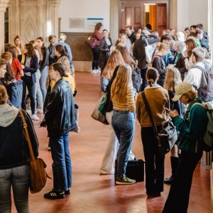 Zahlreiche Studierende warten vor einem Hörsaal und unterhalten sich