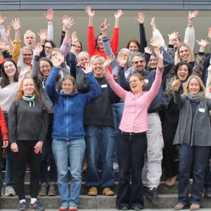 Eine Gruppe von mehr als 25 Personen steht fröhlich auf den Treppen vor dem PH Gebäude und viele strecken ihre Hände in die Luft