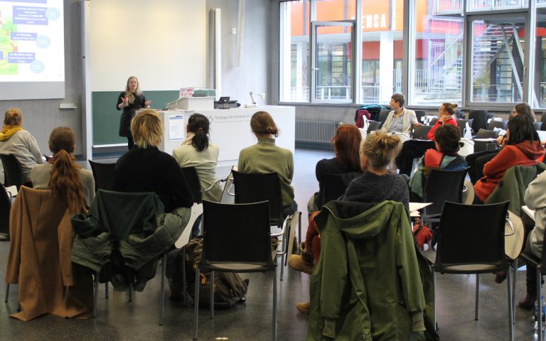 Blick von hinten in einen Seminarraum, in dem gerade ein Workshop stattfindet und die Teilnehmenden einem Input folgen