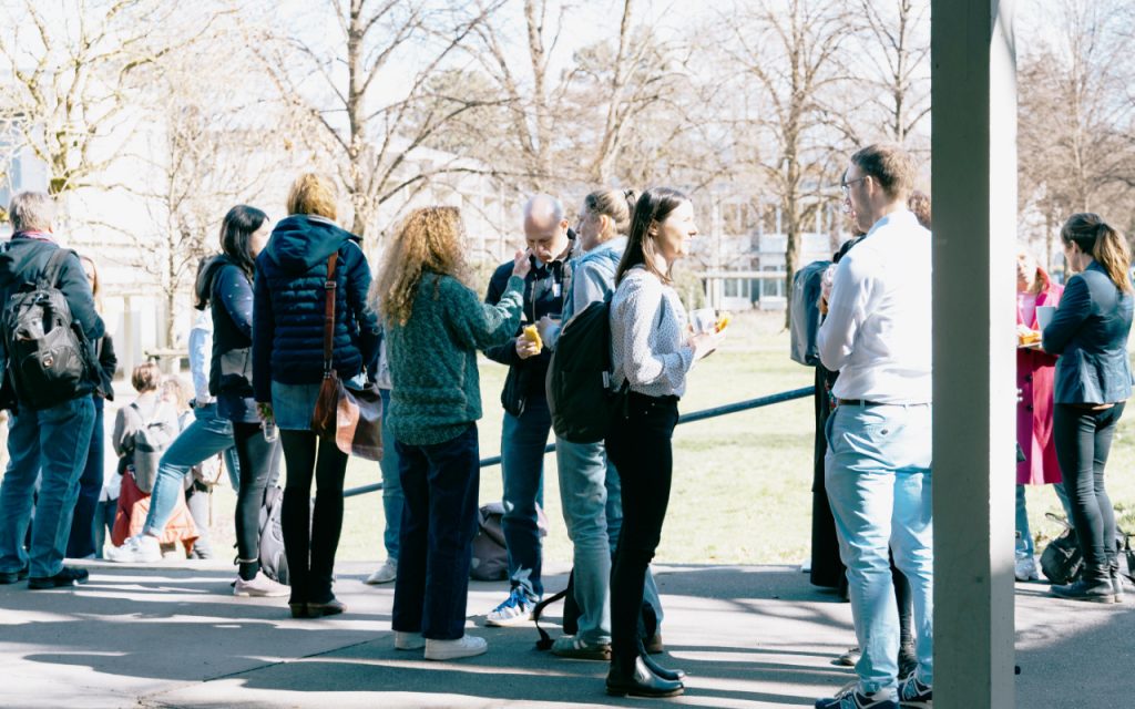 Teilnehmende der Tagung stehen zum Austausch vor der Aula in der Sonne