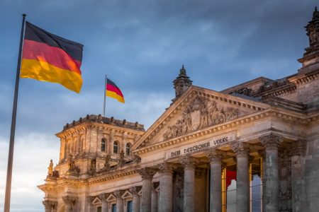 Reichstagsgebäude mit zwei wehenden deutschen Flaggen vor bewölktem Himmel